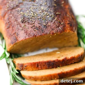 Square image of a perfectly cooked vegan turkey loaf on a white plate, ready to be sliced.