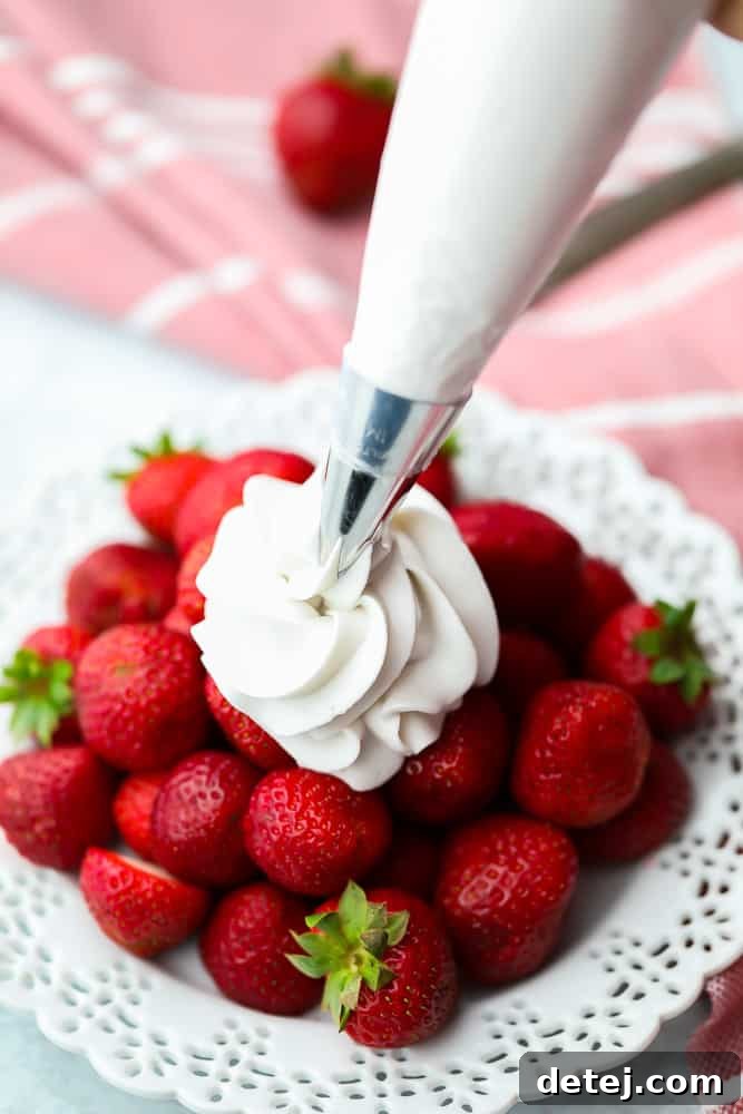 Piping fluffy coconut whipped cream onto fresh, vibrant strawberries, showcasing its perfect texture and appealing presentation.
