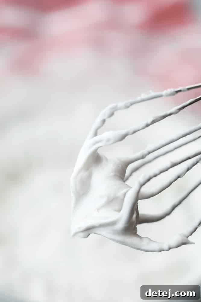 Close-up of coconut whipped cream clinging perfectly to the beaters of a hand mixer, showcasing its thick and stable consistency.