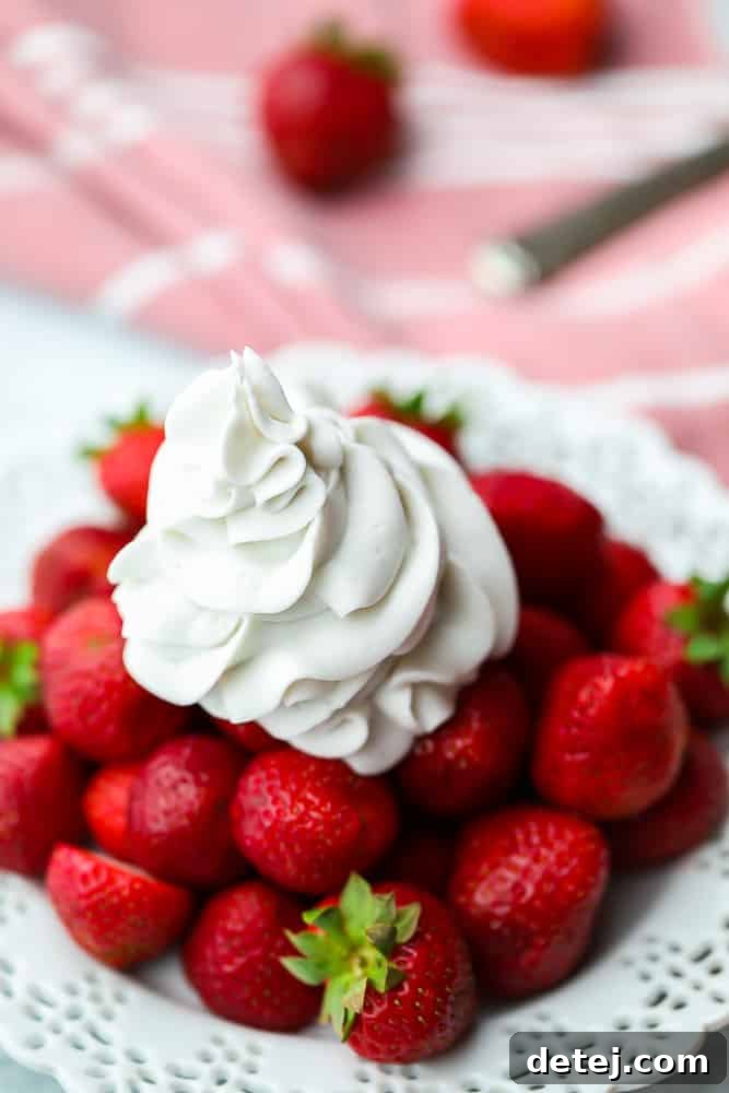 A serving of fresh strawberries generously topped with fluffy coconut whipped cream, artfully arranged on a plate.