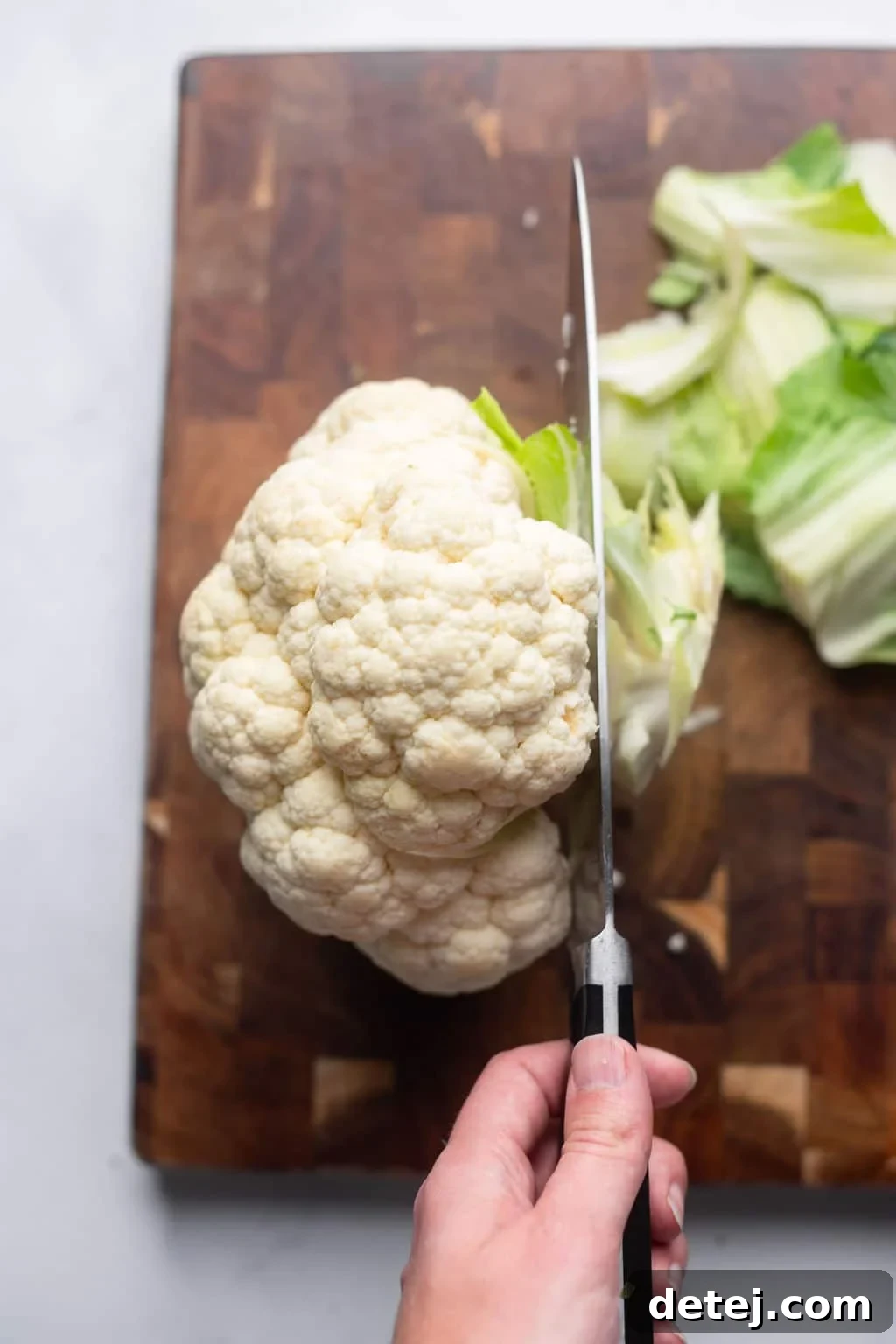 a knife cutting off the stem of a whole cauliflower