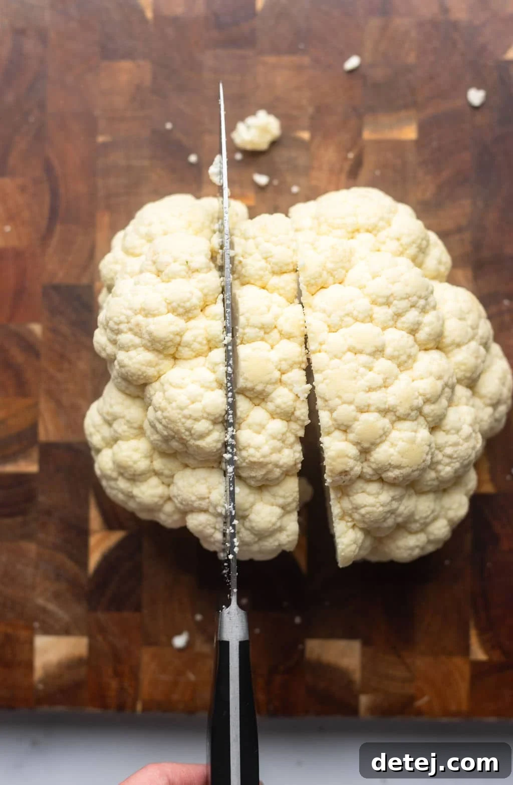 showing a knife cutting slices of cauliflower from whole