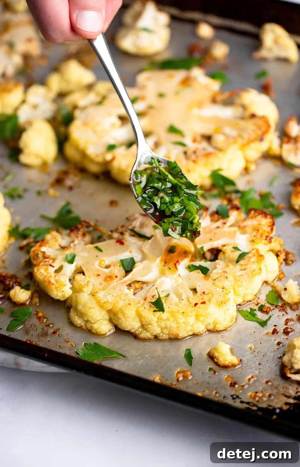 a spoon adding green herbs to roasted cauliflower steaks