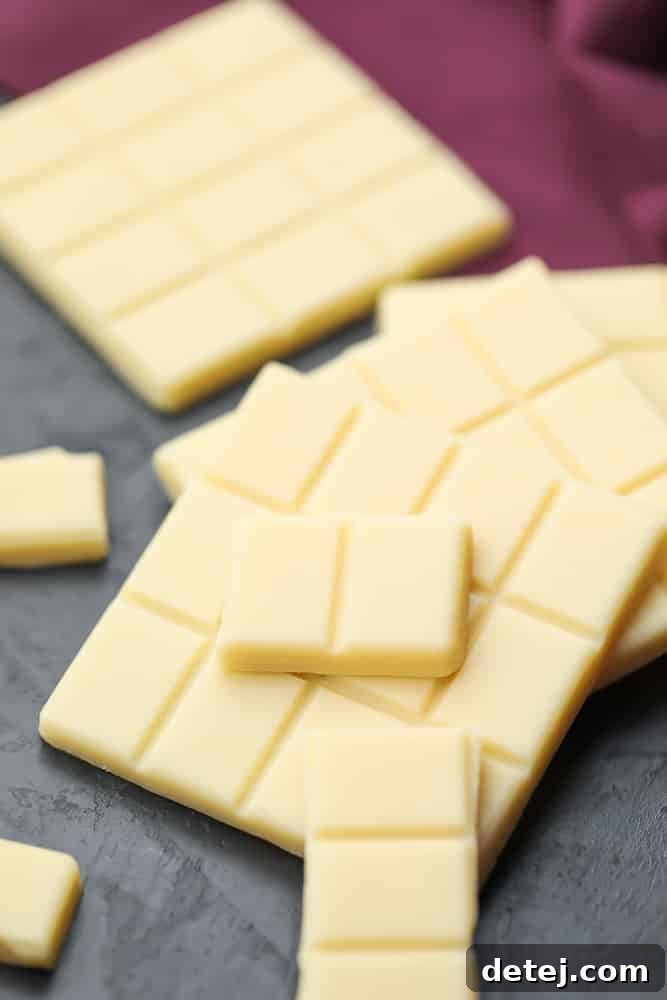 Many broken pieces of vegan white chocolate, laying on top of each other, showcasing its creamy texture.