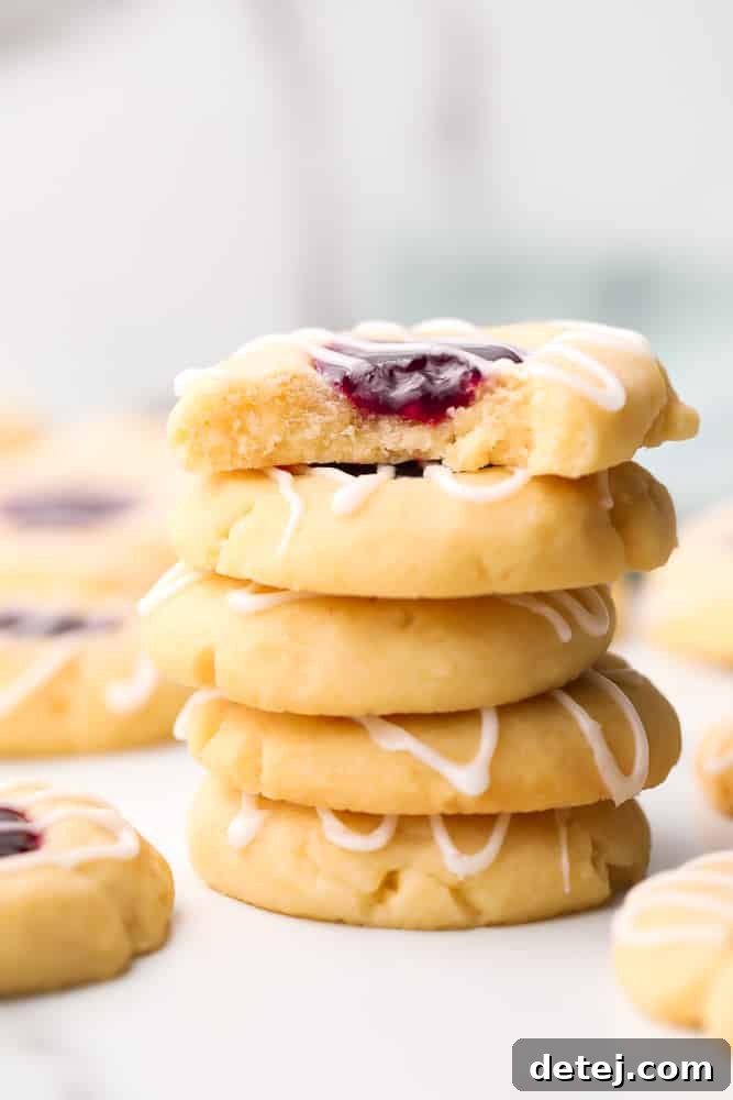 A beautiful stack of vegan thumbprint cookies with vibrant red jam centers, resting on a marble background.