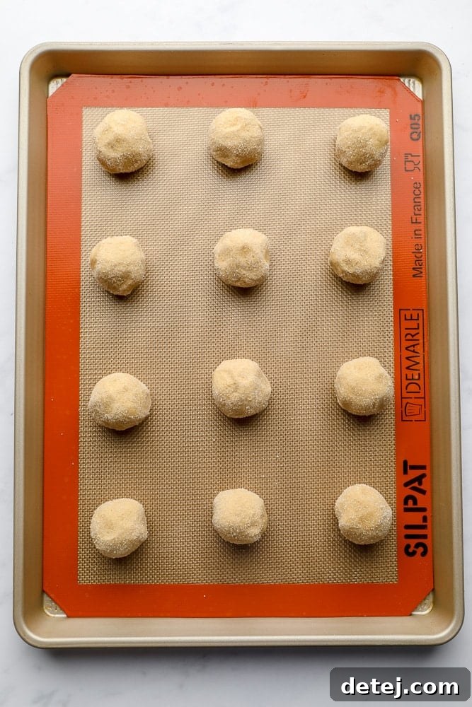 Raw cookie dough balls rolled in sparkling sugar, neatly arranged on a baking sheet, ready for baking.