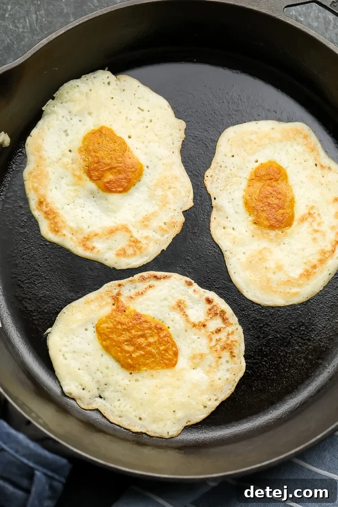 Looking down on three perfectly cooked vegan eggs in a cast iron pan, showcasing their realistic appearance