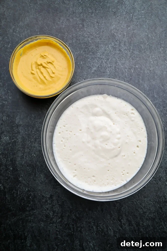 Two bowls on a black background, one with a white tofu mixture and the other with a yellow yolk mixture, ready for cooking