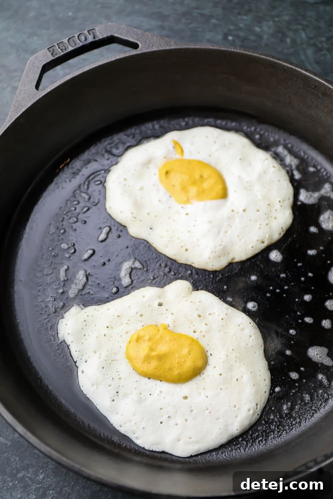 Uncooked white vegan fried eggs with yellow yolks in a pan, ready to be flipped