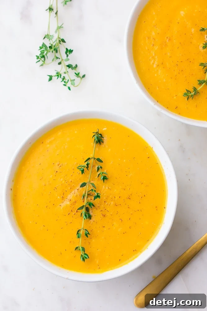 Two bowls of creamy Instant Pot butternut squash soup garnished with fresh thyme, set against a clean white background.