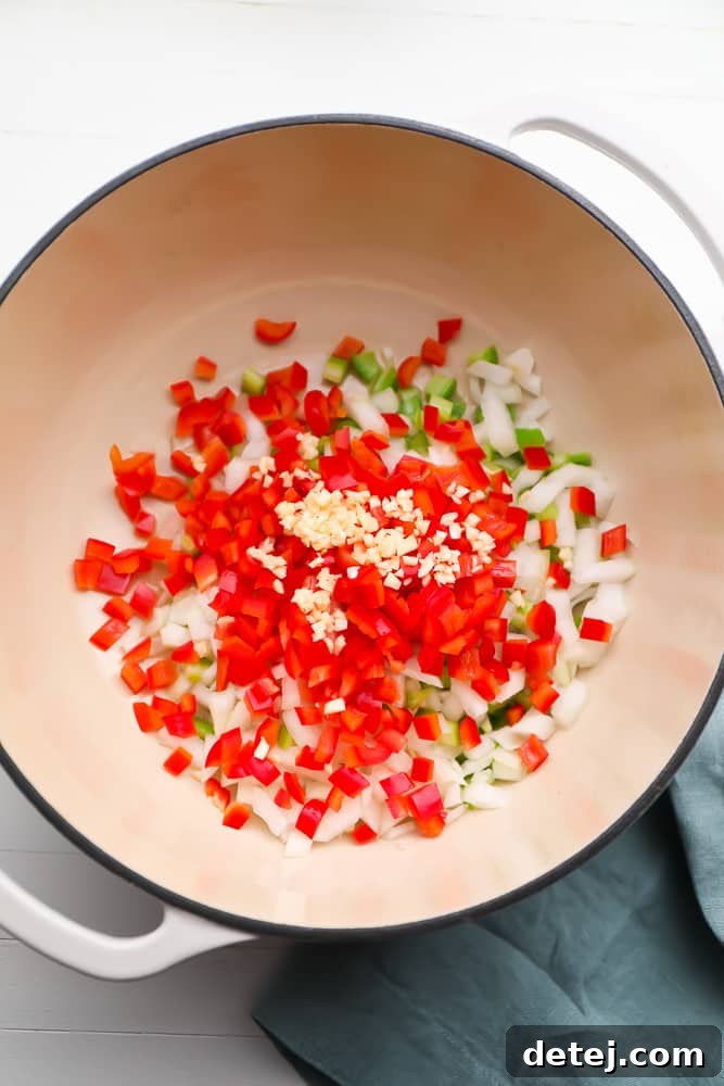 Diced red bell pepper, onion, and celery in a pot, uncooked and ready for sautéing.