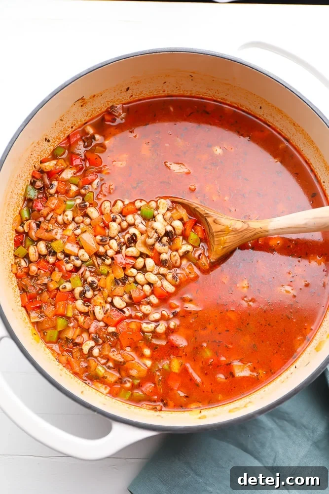 Black eyed peas simmering in a pot with a rich, reddish-brown broth and visible vegetables.