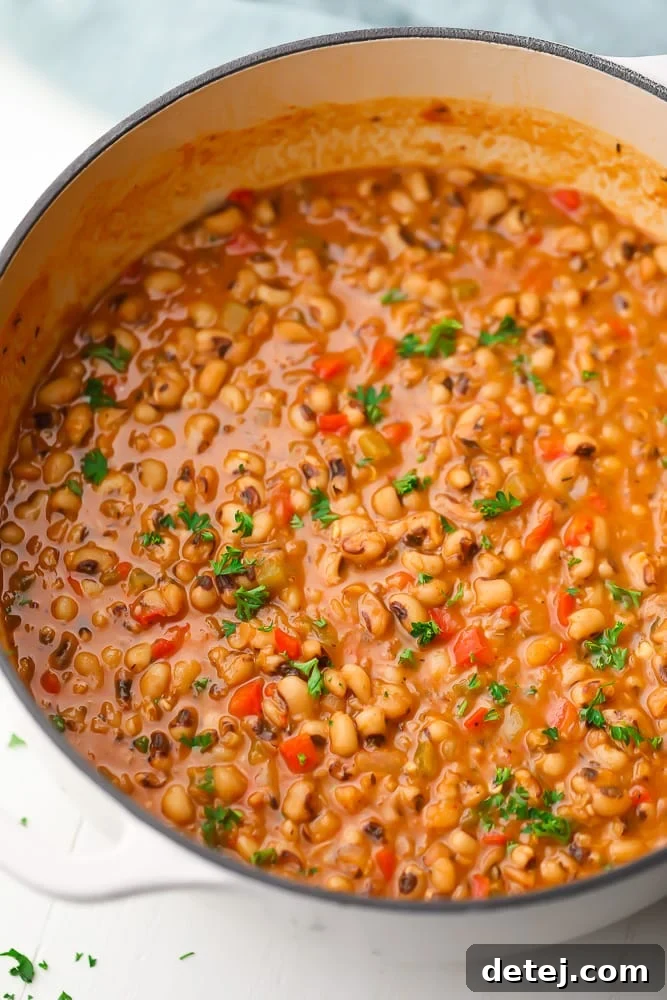 A large white pot filled with cooked black eyed peas, vegetables, and a creamy, light brown broth.