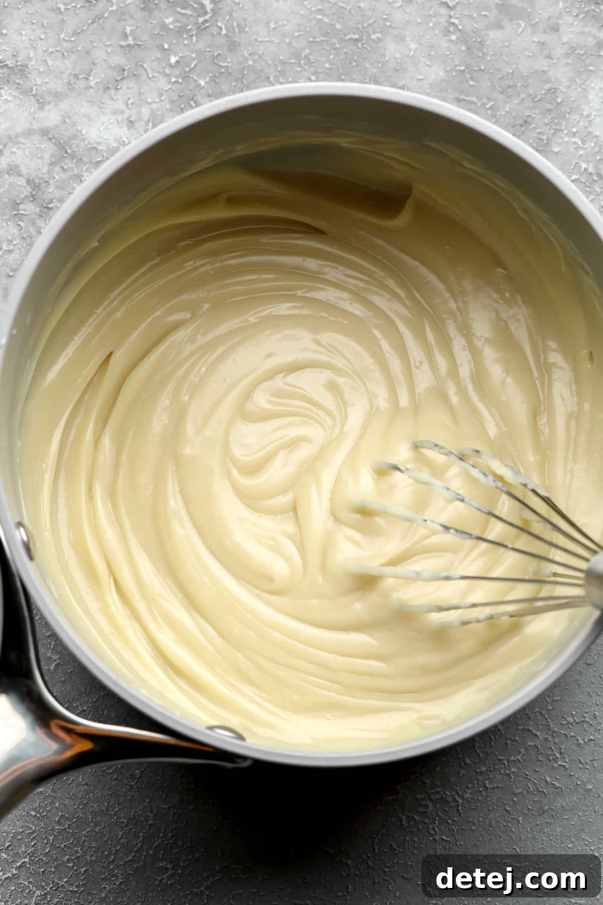 Whisking silky vegan custard in a saucepan, demonstrating the smooth texture during the cooking process.