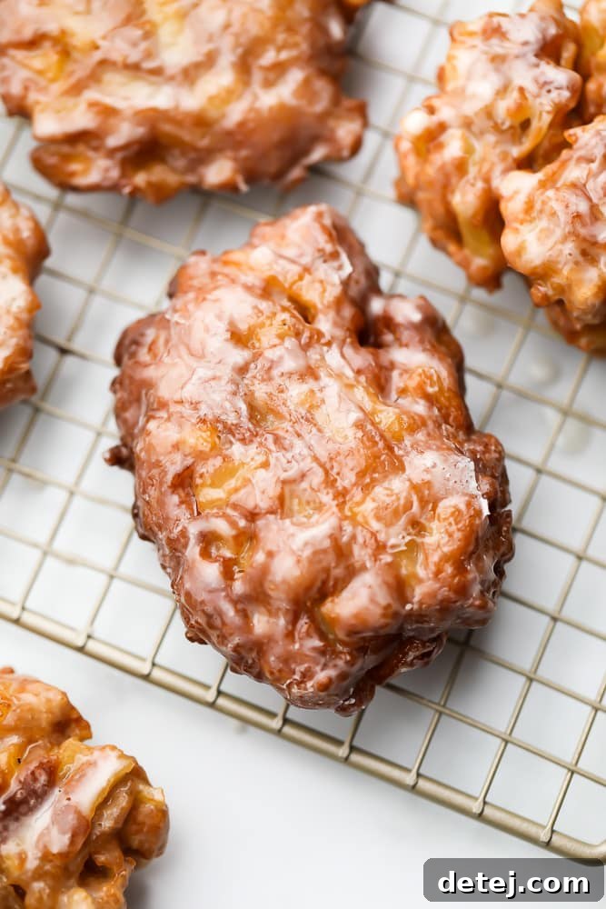 Top-down view of a golden brown apple fritter on a cooling rack, with more fritters visible in the background.