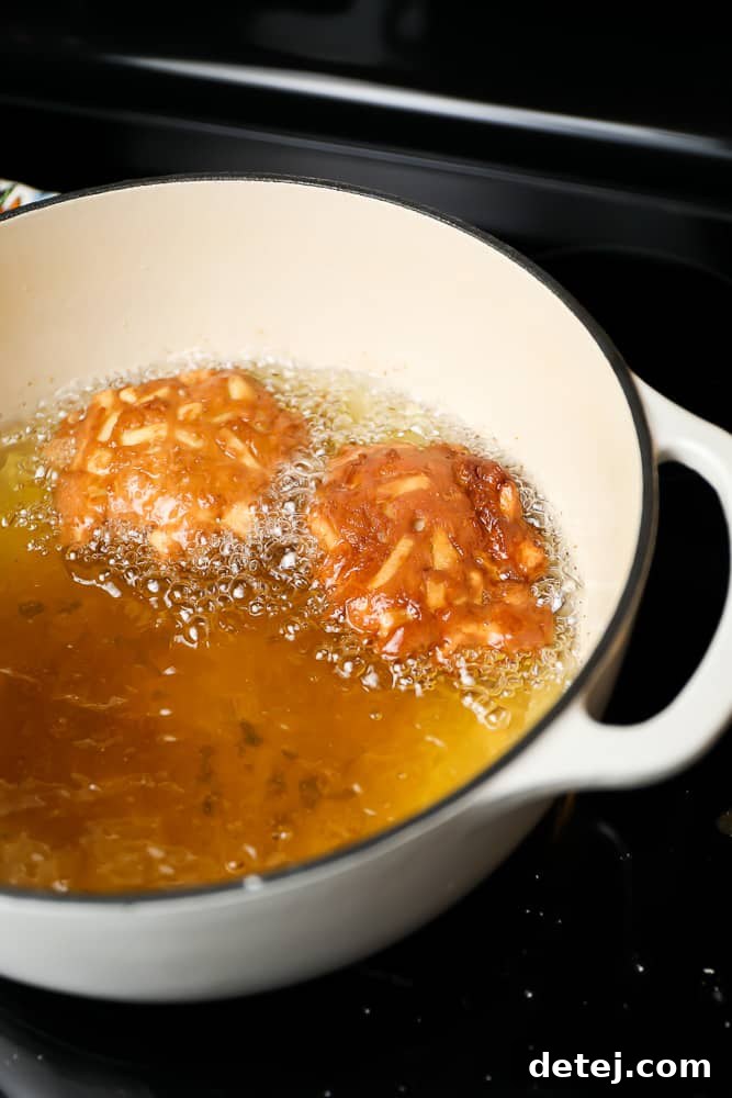 Close-up shot of several apple fritters frying in hot oil in a large deep pot, turning golden brown.
