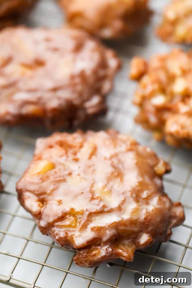A cooling rack filled with many freshly fried and glazed apple fritters, ready to be enjoyed.