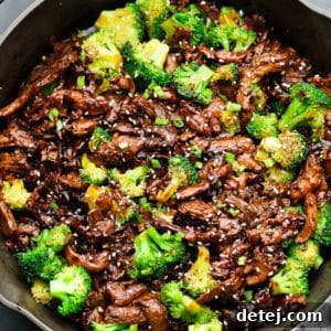 Square image of vegan beef and broccoli in a cast iron pan, garnished with sesame seeds and green onions