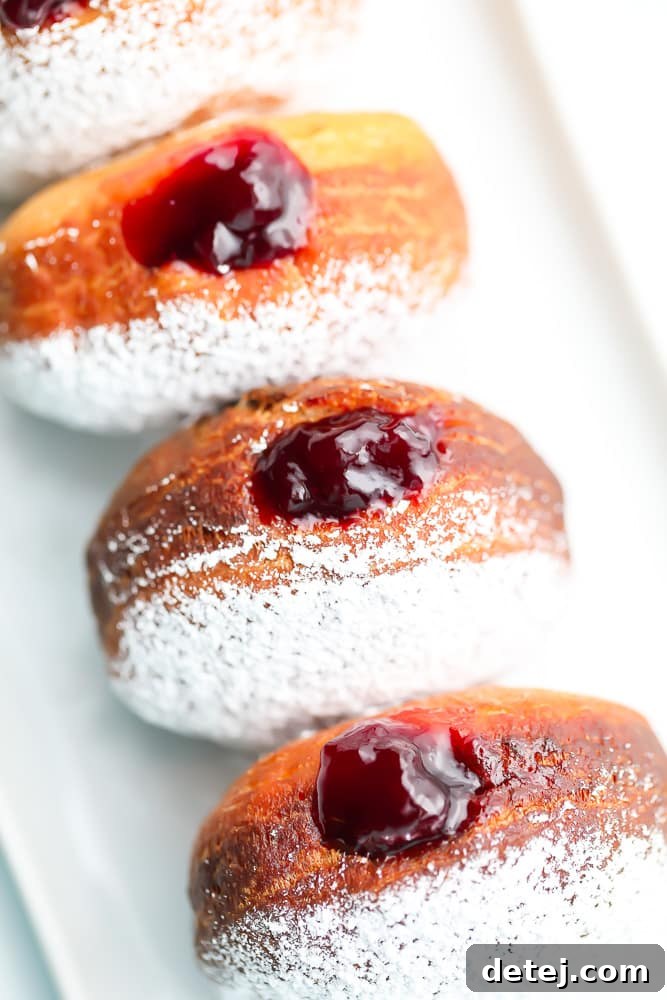 Four golden-brown vegan jelly donuts arranged on their sides, generously dusted with powdered sugar, creating an inviting visual