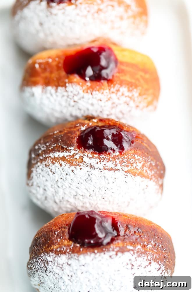 A perfectly arranged straight row of vegan jelly donuts, generously dusted with a fine layer of powdered sugar, showcasing their soft texture and inviting appearance, ready to be enjoyed.