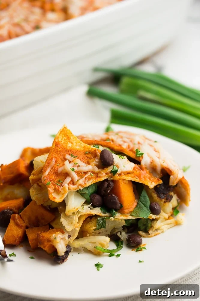 piece of vegan enchilada casserole on a white plate, green onions in background