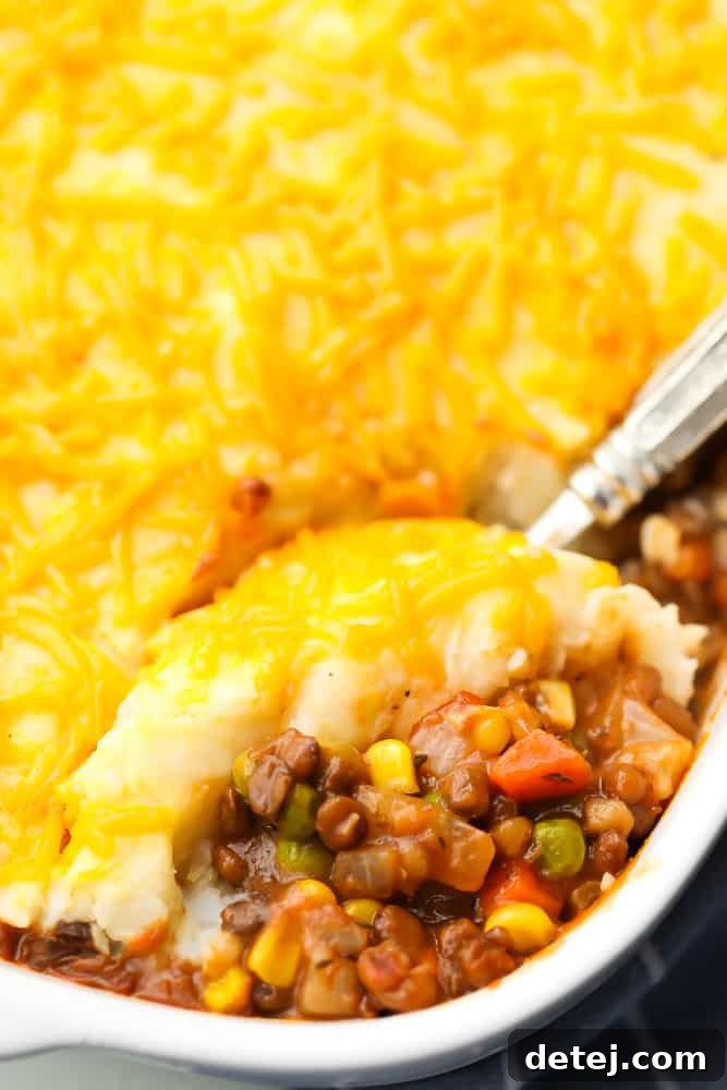 A golden-brown vegan lentil shepherd's pie served in a rustic casserole dish, with a large spoon scooping out a generous portion, showcasing the fluffy mashed potato topping and rich lentil base.