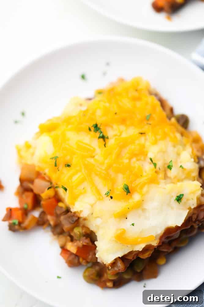 A perfectly portioned square of vegan lentil shepherd's pie sits on a white plate, showcasing the distinct layers of creamy mashed potatoes and rich, earthy lentil filling.