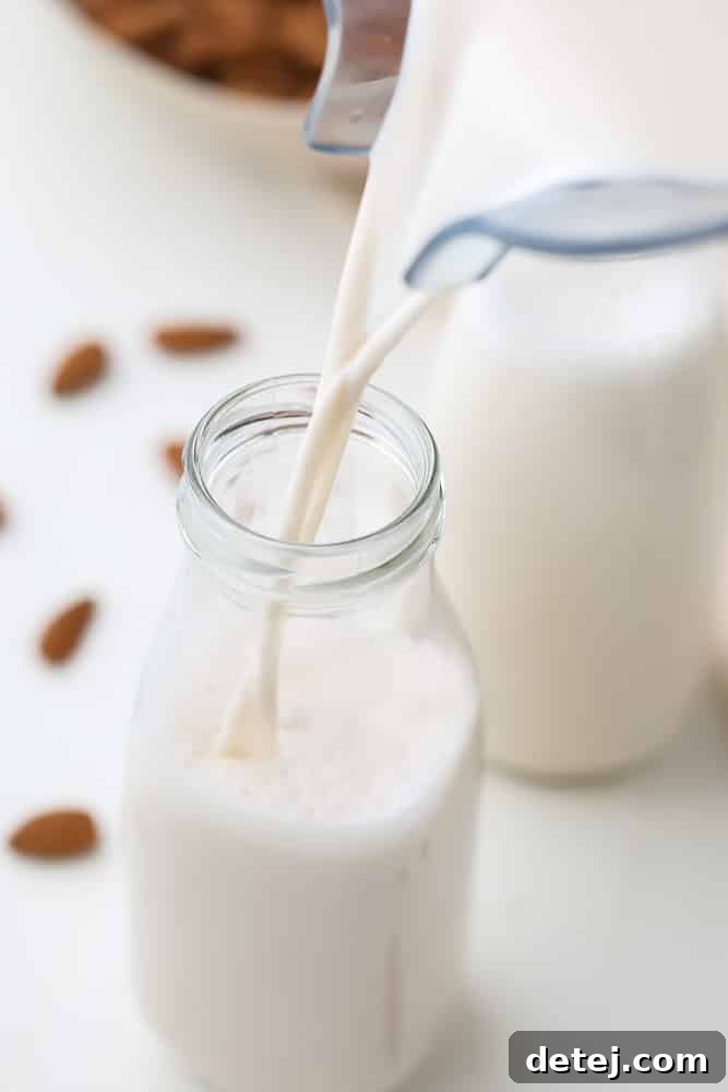 Freshly blended almond milk pouring into a clear glass bottle from a blender
