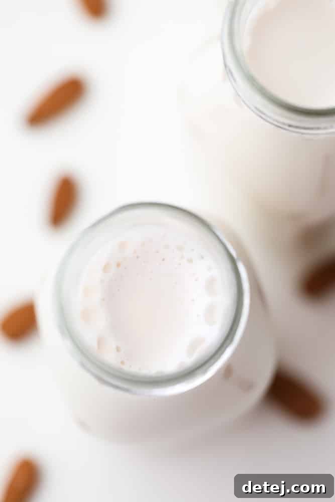 Overhead view of a glass bottle of white almond milk with raw almonds scattered in the background