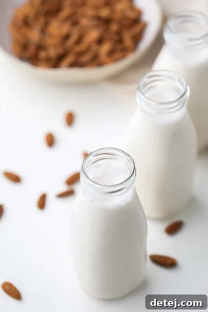Two glass milk bottles filled with white almond milk, with raw almonds scattered around them