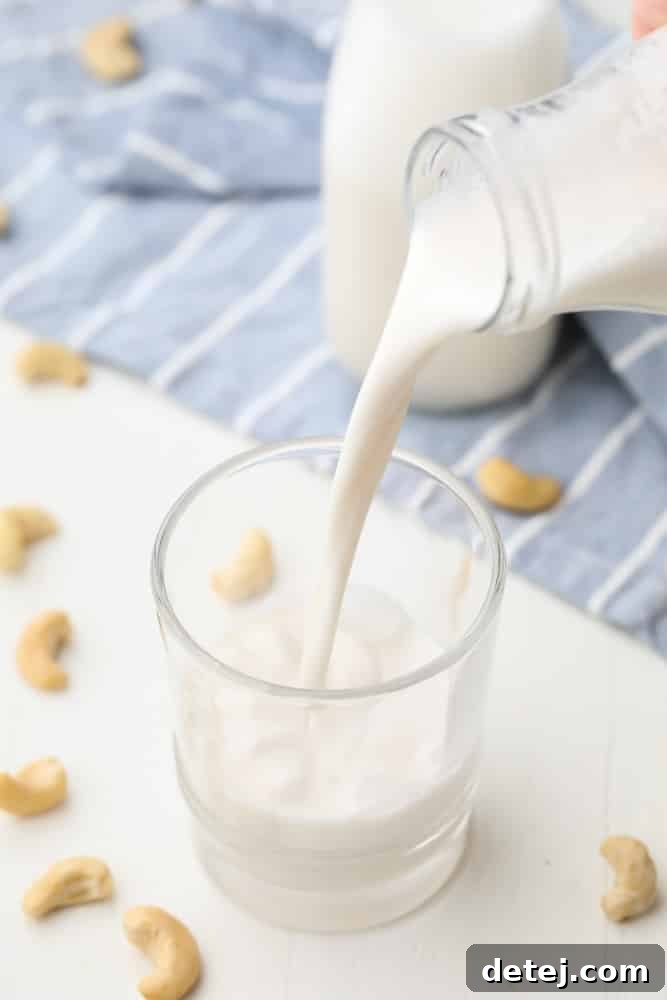 white milk with cashews in background being poured into cup