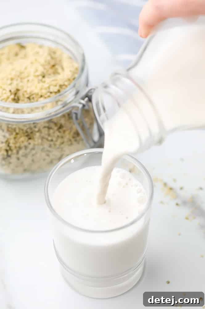 Freshly made hemp milk pouring into a glass, with hulled hemp seeds scattered in the background