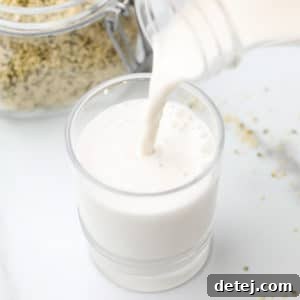 Square image of creamy hemp milk pouring into a cup, with hemp seeds in the background