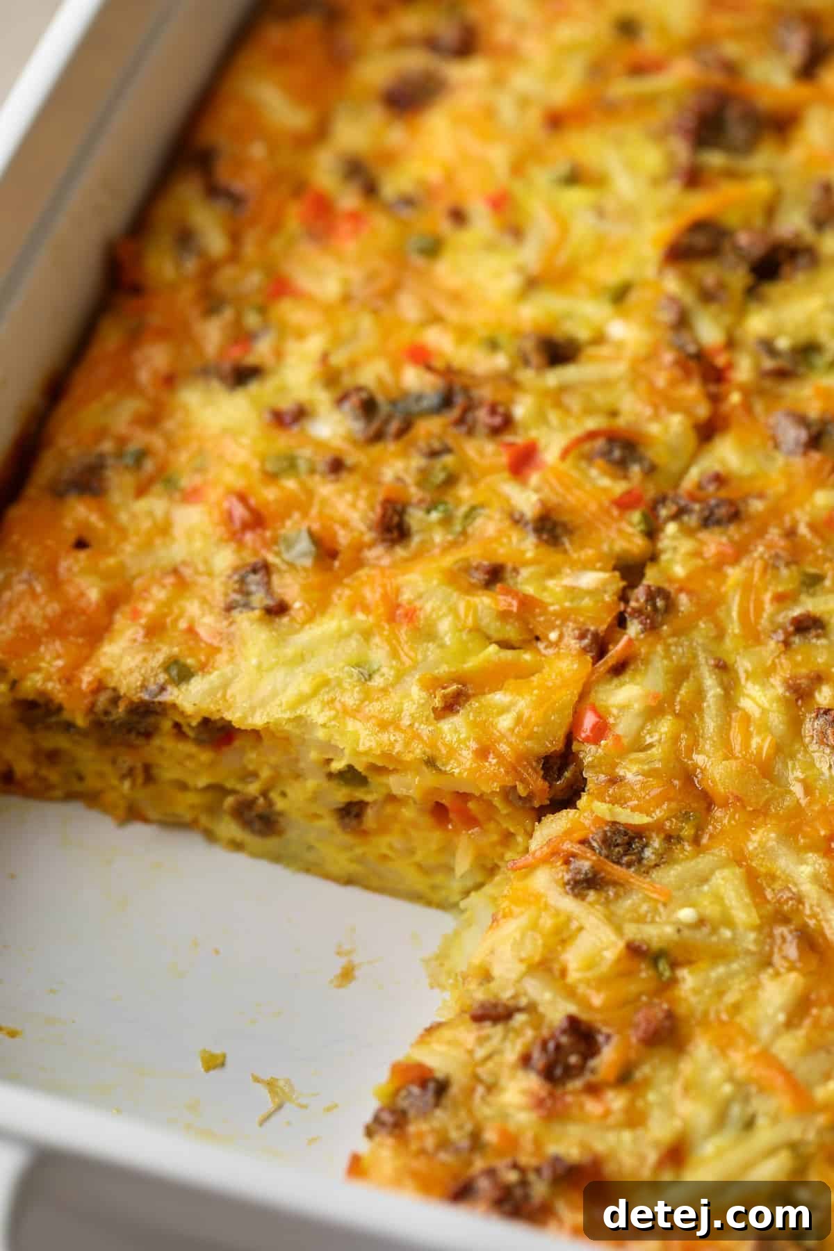 A perfectly sliced vegan breakfast casserole in a baking dish, showcasing layers of hash browns, vegetables, and fluffy vegan egg mixture.