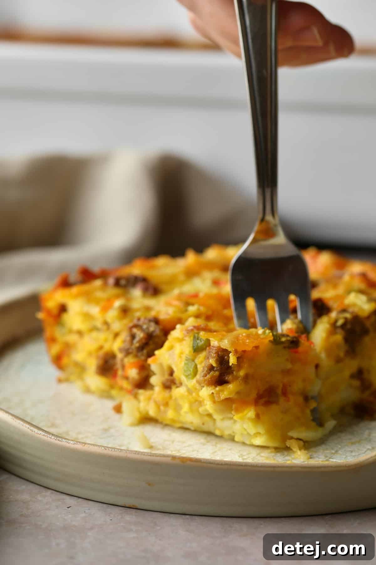 A fork taking a delicious bite out of a warm slice of vegan breakfast casserole, highlighting its fluffy texture.