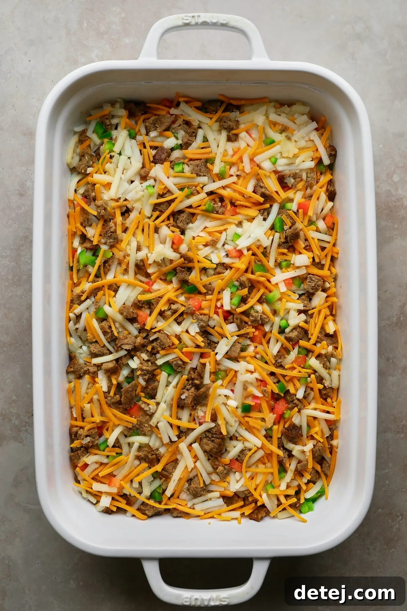 The colorful filling for a vegan breakfast casserole, featuring hash browns, vegan sausage, and various vegetables in a white baking dish, ready for the egg mixture.