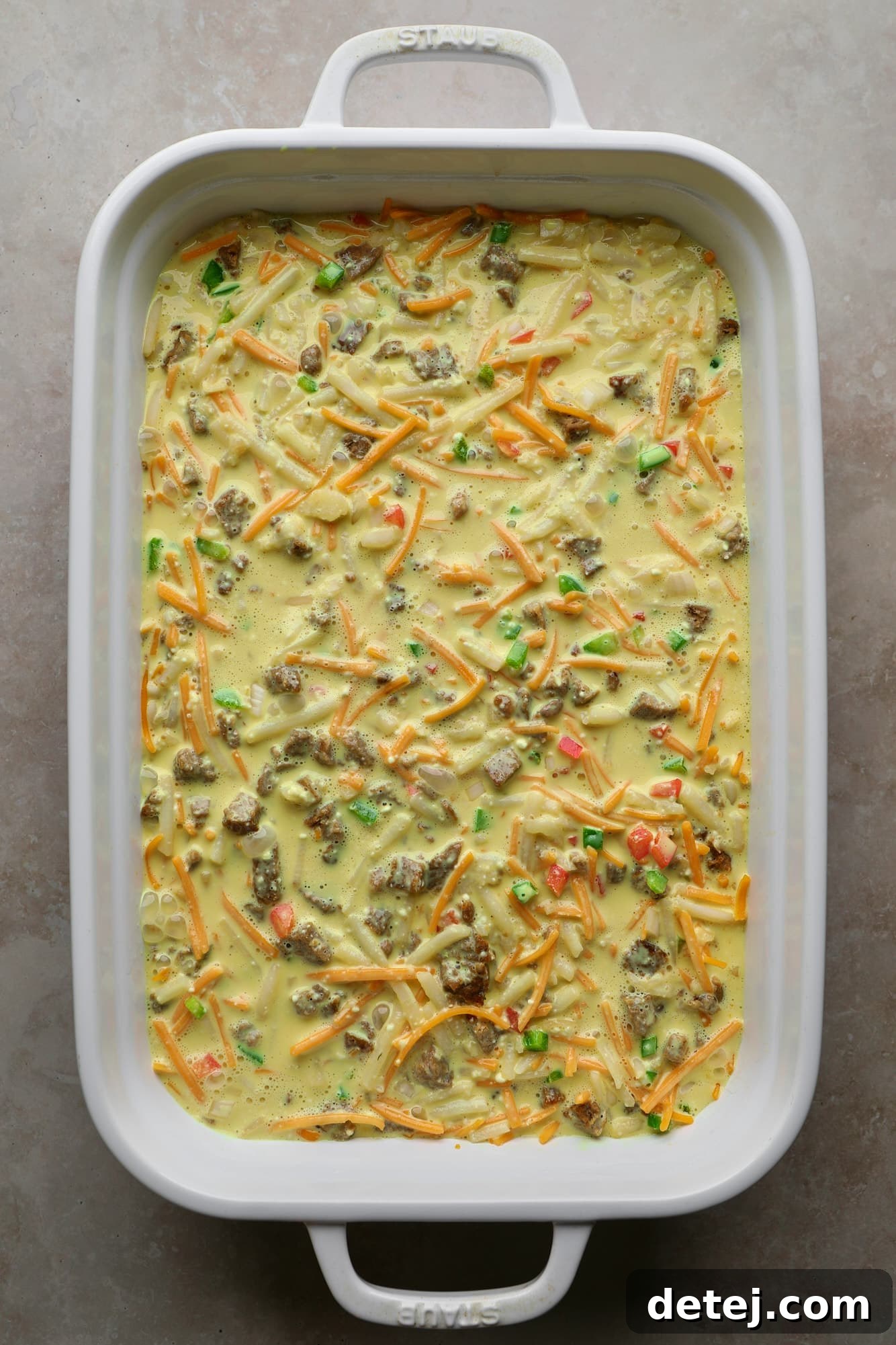 An assembled and unbaked vegan breakfast casserole in a white baking dish, with the vegan egg mixture poured over the solid ingredients, ready for baking.