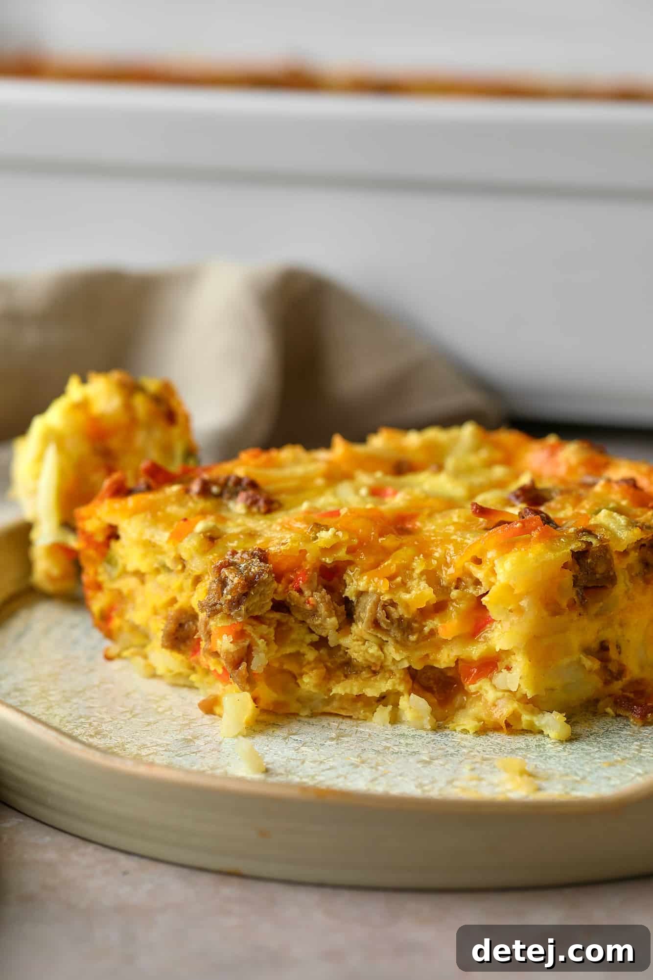 A close-up shot of a slice of Vegan Breakfast Casserole on a white plate, with a bite removed, revealing the inner layers and fluffy texture.