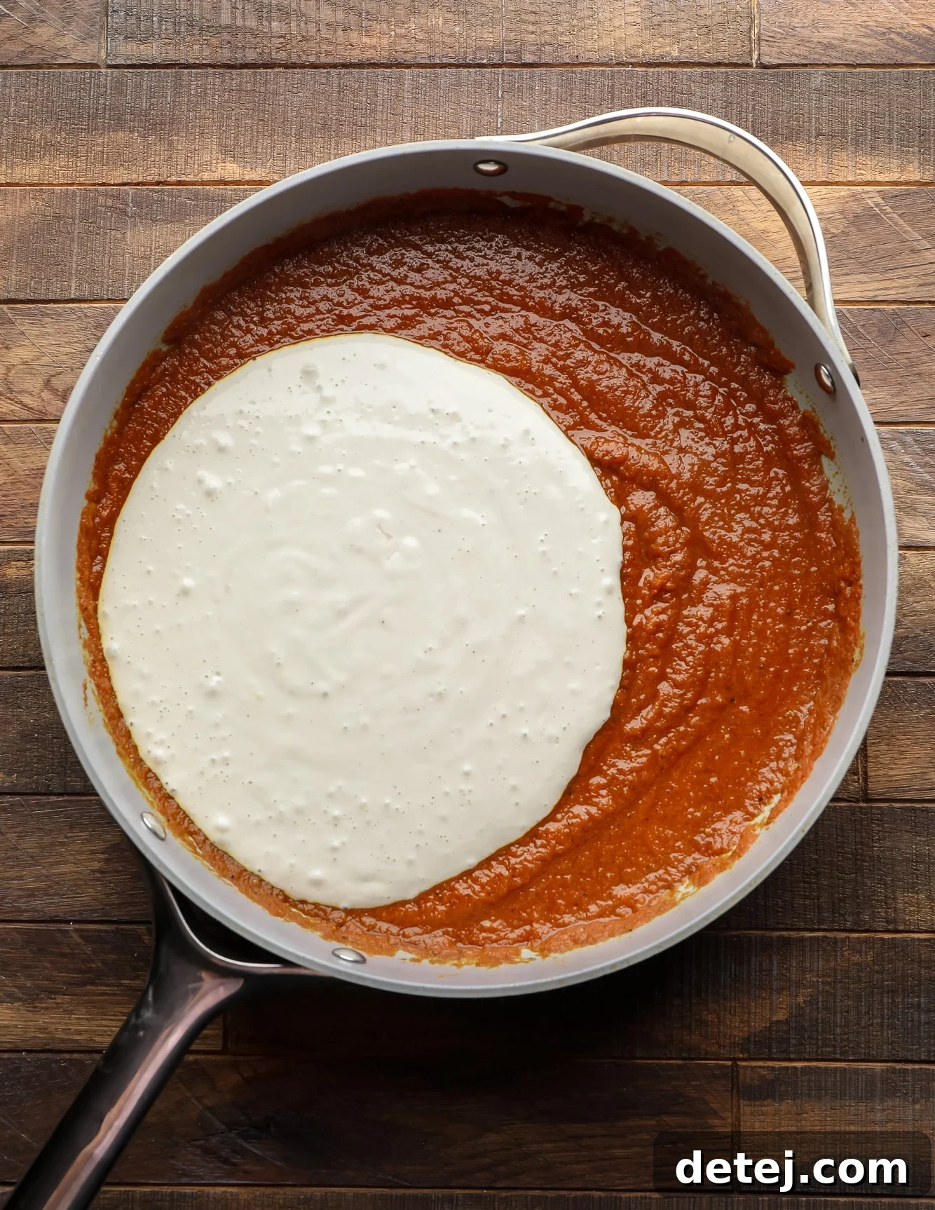 white cashew cream poured into a skillet with tomato puree.