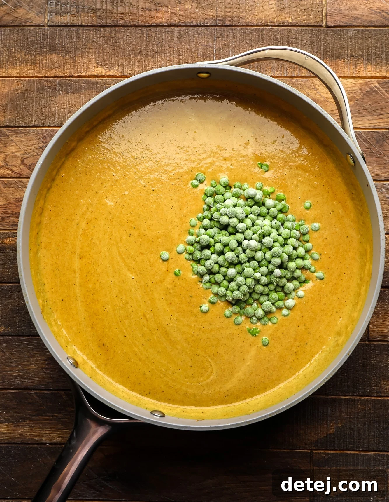 a pile of frozen peas in a yellow sauce in a large skillet.
