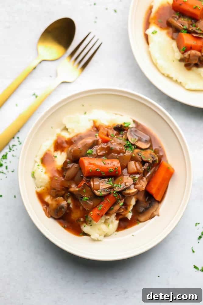 A white bowl with mashed potatoes and a vegetable stew on top