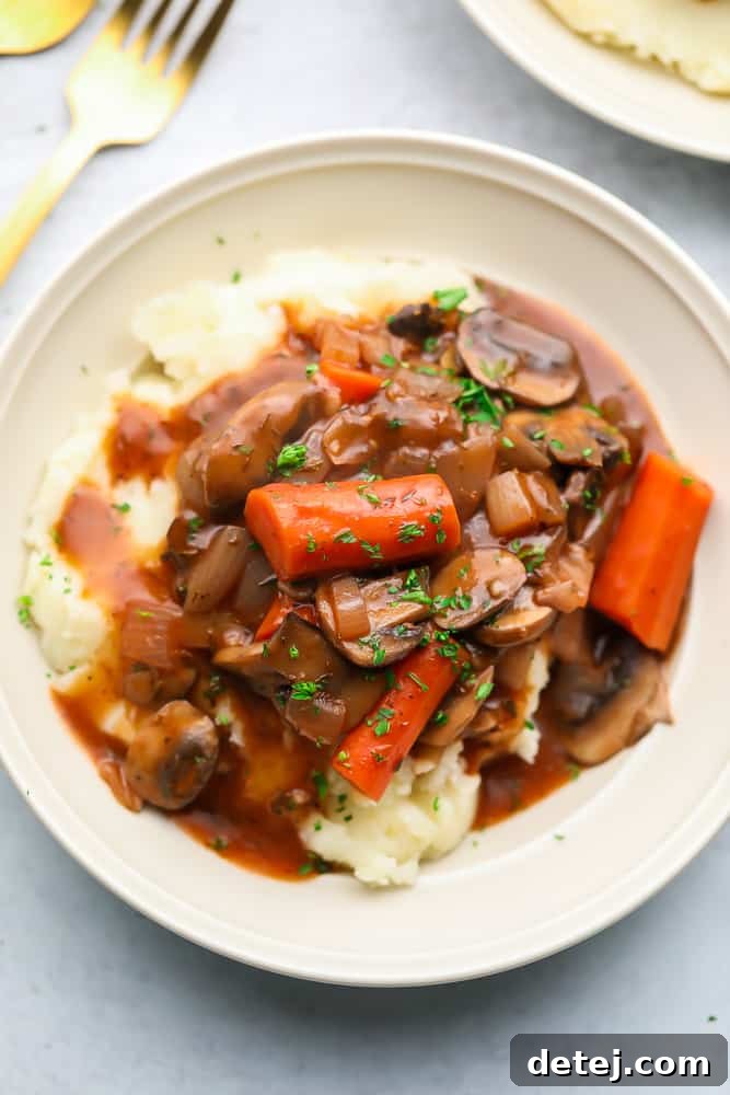 Close up of a white bowl with mashed potatoes and a mushroom and vegetable stew on top