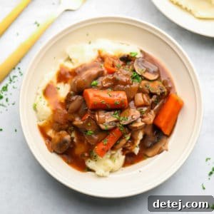 A white bowl with mashed potatoes and a vegetable stew on top