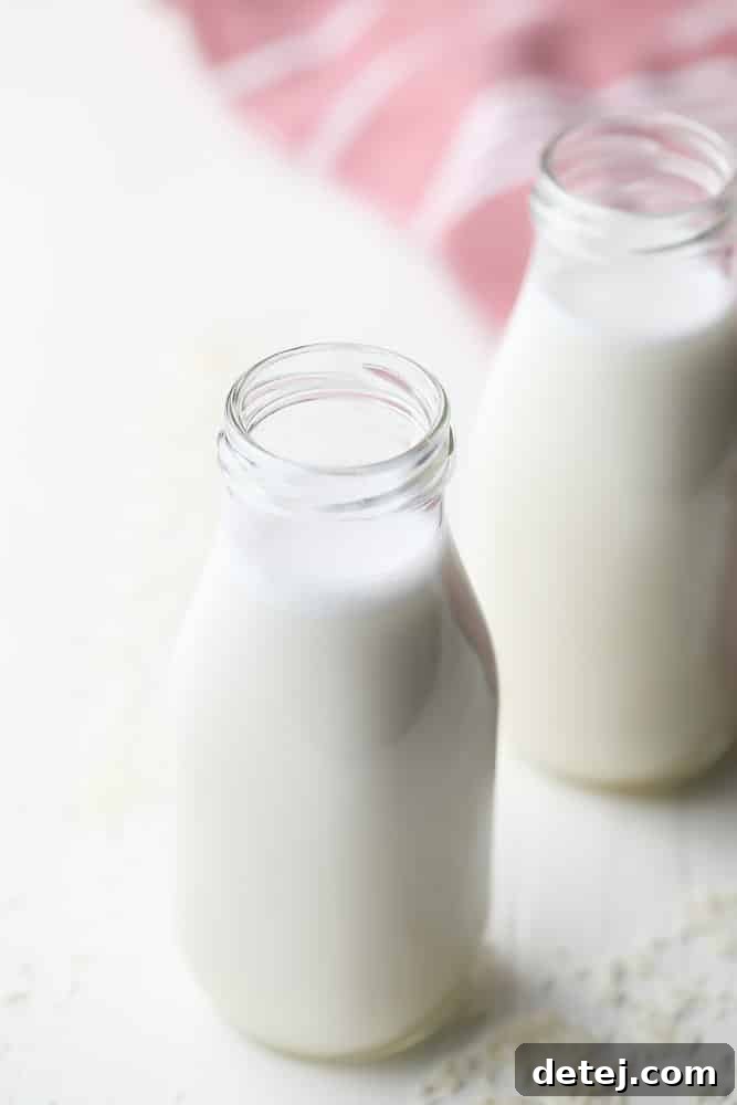 Two glass bottles filled with freshly made creamy coconut milk, with loose coconut flakes scattered around them, ready for refrigeration.