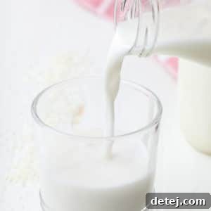 Square image of a glass of milk being poured into a cup from a jar, representing homemade coconut milk.