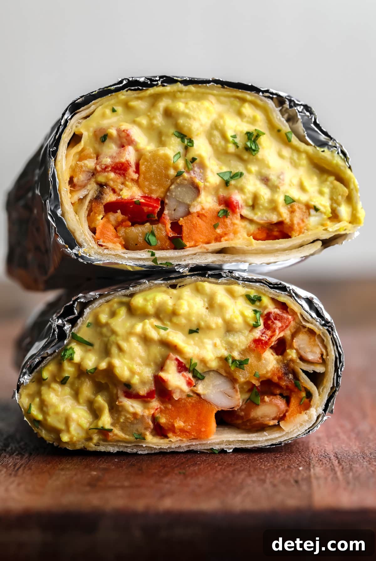 burrito cut in half with foil around it on wood board with eggy mixture plus veggies