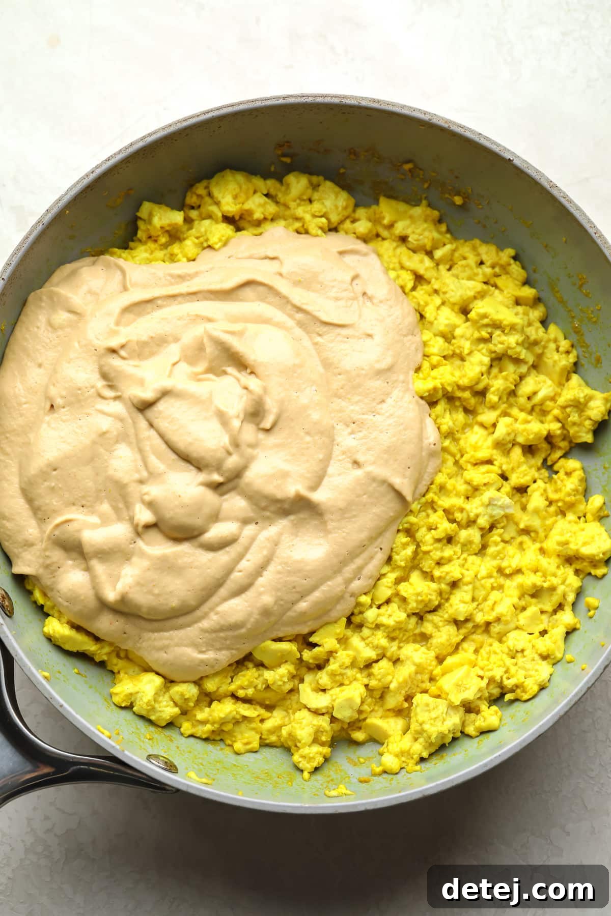 tofu scramble yellow with creamy sauce being added to a pan