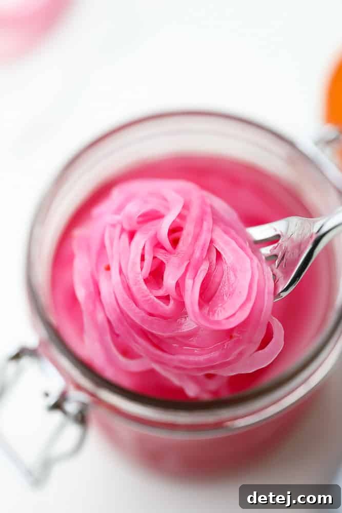 Tangy Ruby Onions 2 close up of a fork taking a scoop of pickled red onions out of a mason jar