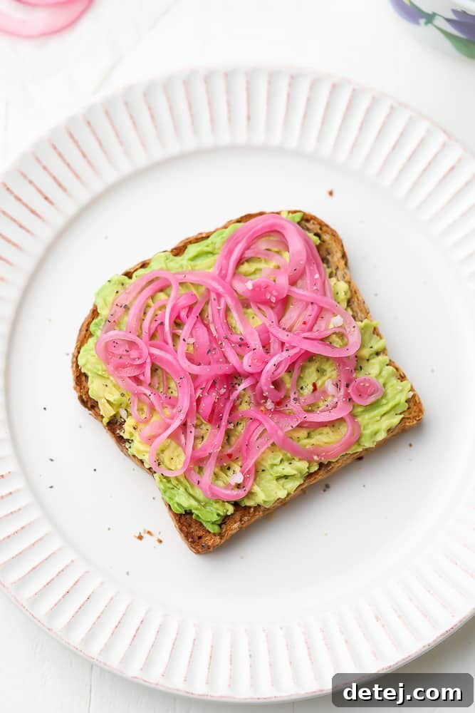 Tangy Ruby Onions 6 slices of pickled red onions on a piece of avocado toast on a white plate