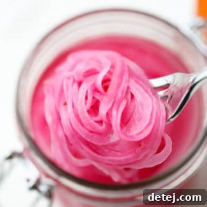 Tangy Ruby Onions 7 close up of a fork taking a scoop of pickled red onions out of a mason jar
